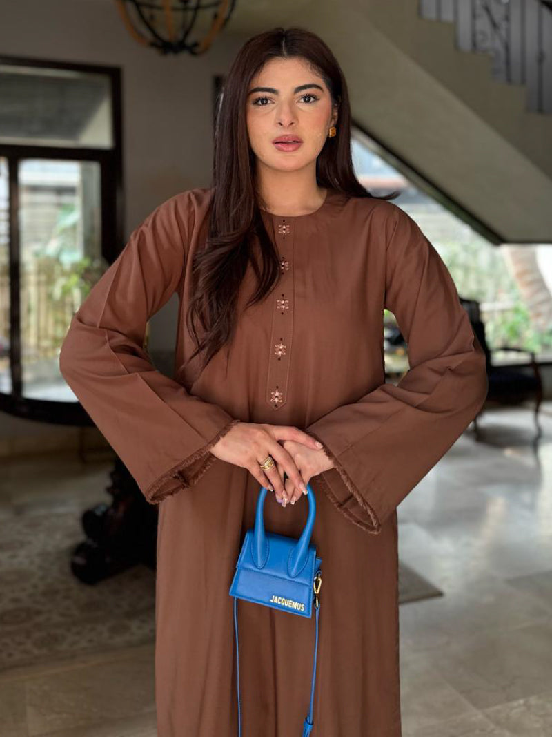 A model wears a coffee-brown A-line kurta with intricate embroidery on the patti. She is holding a small blue handbag.